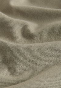 Tissu beige doux avec une texture fine en maille, présenté en plis délicats et un éclairage subtil mettant en valeur sa surface lisse.