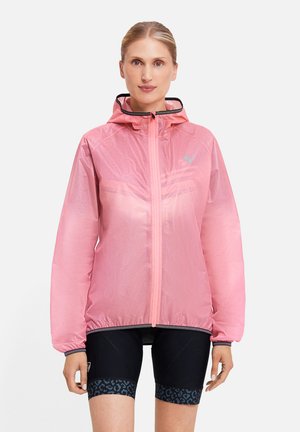 Woman wearing a light pink hooded jacket zipped up, with black cycling shorts featuring a dark blue leopard pattern on the hem.