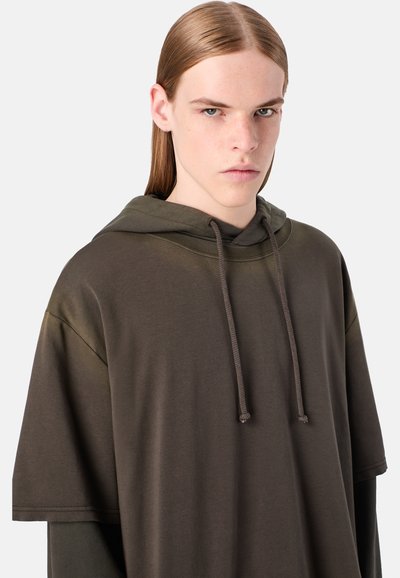 Felpa con cappuccio di color verde oliva scuro, realizzata in materiale morbido. Presenta una vestibilità ampia, maniche larghe e dettagli con cordoncino.