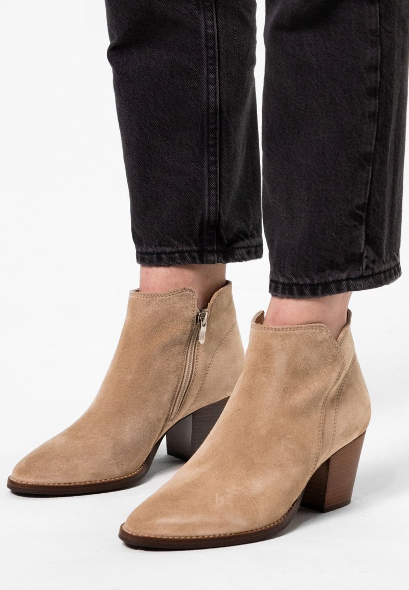 Beige Wildleder-Ankle-Boots mit spitzer Zehenform, Reißverschluss an der Seite und einem gestapelten Holzabsatz, kombiniert mit schwarzen, cropped Jeans.