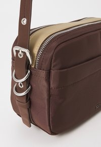 Borsa a tracolla in nylon marrone con una cerniera dorata, dettagli in metallo e tracolla regolabile; presenta una tasca frontale e una texture liscia.