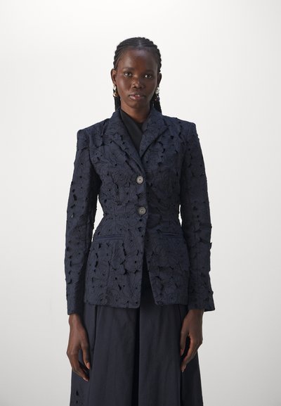 Navy blue blazer with floral lace texture, two front buttons, notched lapels, and pockets. Styled with a black top underneath.