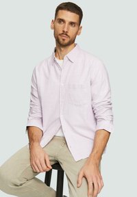Lichtpaarse overhemd met knopen en een borstzak, lange mouwen opgerold, gestructureerde stof, gedragen over een witte ronde hals t-shirt, in combinatie met beige broeken.