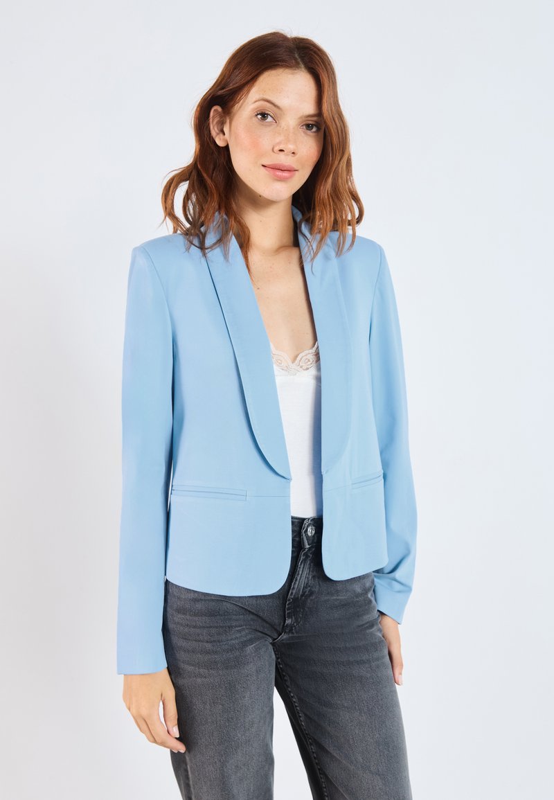 Blazer ajusté bleu clair avec un col cranté, une fermeture à un bouton à l'avant et deux poches avant. Porté sur un débardeur en dentelle blanche et un jean foncé.