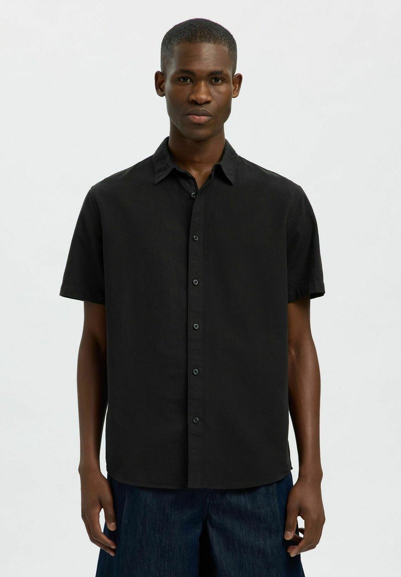 Camisa de manga corta en tejido negro sólido. Cuenta con un cierre de botones en la parte delantera, cuello puntiagudo y un corte relajado. Textura suave con un ligero brillo.