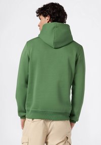 Felpa verde con una texture morbida, cappuccio regolabile e polsini a coste. Design a taglio dritto e superficie di tessuto semplice. Abbinata a pantaloni cargo beige.