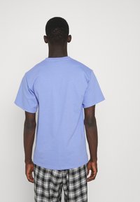 Kratký rukáv, tričko s kulatým výstřihem v světle modré barvě z bavlny. Zadní pohled ukazuje uvolněný střih s hladkou texturou, bez ozdob.