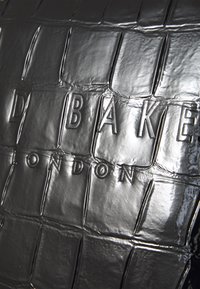 Textura de cuero negro grabado con el texto "D B A K E LONDON" en letras en relieve y brillantes sobre un patrón de cuadrícula.