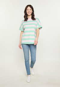 Stripet t-shirt i grøn og pink bomuld, korte ærmer, afslappet pasform, paret med lyseblå skinny jeans og hvide sneakers.