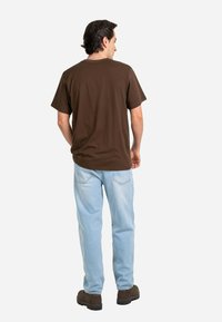 Camiseta de algodón marrón de mangas cortas, combinada con jeans de mezclilla azul claro. El conjunto se completa con zapatos marrones oscuros.