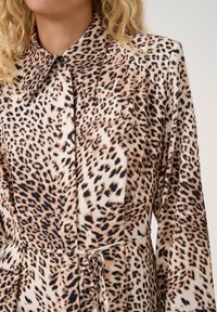 Abito con stampa leopardata, caratterizzato da un colletto classico, maniche lunghe e vita con coulisse. Realizzato in tessuto liscio e leggero con fantasie variate.