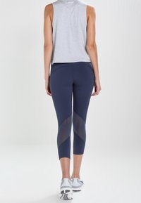 Leggings azul marino con paneles de malla, corte a la altura del tobillo y textura suave, combinados con una camiseta sin mangas gris y zapatos deportivos blancos.