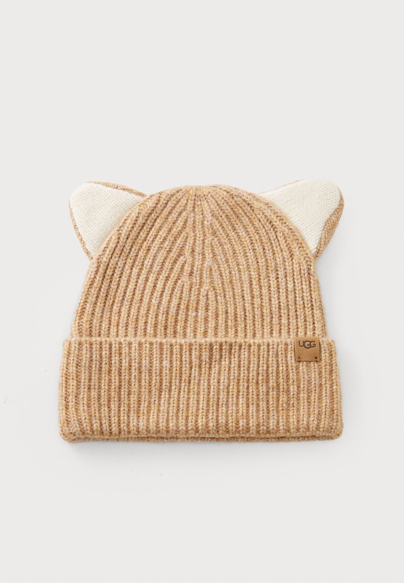 Bonnet en beige avec texture côtelée, présentant des oreilles de chat blanches sur le dessus et un petit patch en cuir avec marque sur le côté.