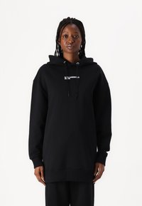 Black hoodie made of cotton, featuring a front kangaroo pocket, drawstring hood, and embroidered logo text in white. Relaxed fit with ribbed cuffs.