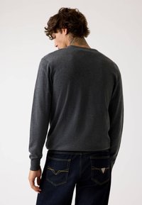 Maglione grigio a maniche lunghe con scollatura rotonda, realizzato in materiale morbido. Abbinato a jeans in denim scuro con cuciture gialle.