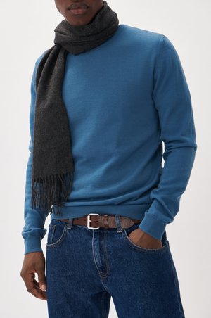 Blue long-sleeve knit sweater paired with a dark gray scarf, featuring fringe edges. Worn with brown leather belt and blue denim jeans.