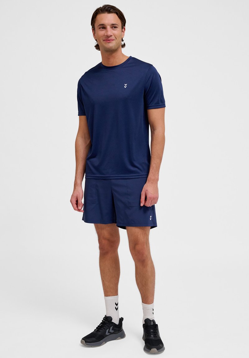 Marinblå idrottströja och shorts, korta ärmar, slät tyg, logotyp på bröstet, kombinerat med svarta sneakers och vita strumpor med mönster.