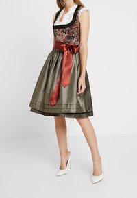 Bloemmotief top met kantafwerking, taille met satijnen strik. Metalen gouden, geplooide rok. Model draagt witte hakken.
