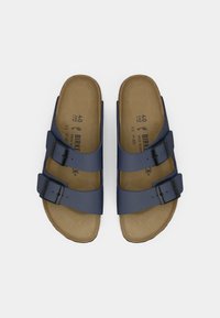 Une paire de sandales Birkenstock bleu marine avec deux sangles ajustables et des boucles noires sur des semelles en liège beige, vue de dessus.
