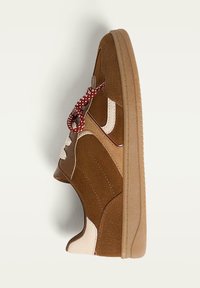 Sneaker in suede marrone con accenti crema, pannelli laterali texturizzati e un laccio a trama rossa e bianca. Presenta una punta rotonda e suola in gomma.