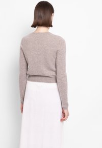 Světle hnědý svetr s dlouhými rukávy, měkkou texturou, žebrovaným lemem a kulatým výstřihem, zkombinovaný s bílou sukní až ke kotníkům.