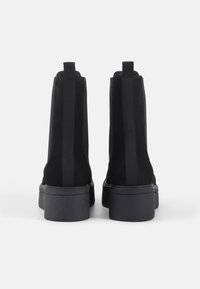 Černé semišové boty s elastickými bočními panely a chunky podešví. Design se vyznačuje hladkým povrchem a minimalistickou konstrukcí.