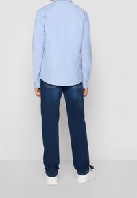 Hellblaues Langarmhemd mit geradem Schnitt und Knopfmanschetten, kombiniert mit dunkelblauen Jeans und weißen Sneakern.