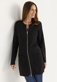 Svart lång cardigan med dragkedja framtill, två framfickor och rund halsringning. Tyget ser slätt och strukturerat ut.