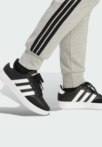 Mustat ja valkoiset lenkkarit, joissa on kolme tunnusomaista raitaa, valmistettu nahasta ja mokasta, yhdistetty harmaisiin collegehousuihin, joissa on mustat sivuraidat.