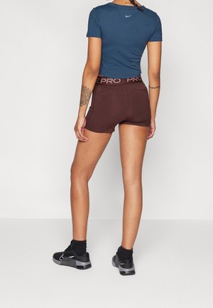 Mujer de espaldas a la cámara, vestida con camiseta Nike azul marino, pantalones cortos Nike Pro marrones, calcetines negros y zapatillas Nike negras.