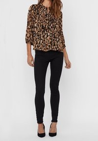 Blouse à motifs marron et noir avec un design plissé, associée à un jean skinny noir et des talons hauts noirs.