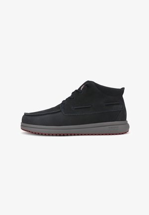 Des bottes chukka en suède noir présentent un profil bas, un bout arrondi, une semelle en caoutchouc grise avec un motif de traction rouge, et un design à lacets.