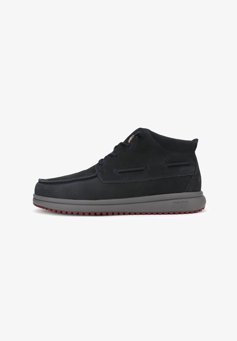 Des bottes chukka en suède noir présentent un profil bas, un bout arrondi, une semelle en caoutchouc grise avec un motif de traction rouge, et un design à lacets.