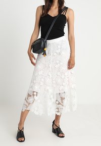 Vit spetsskjol i midi-längd med blommönster, kombinerad med en svart linne-top och en liten svart axelväska. Svarta klacksandaler med blockklack.