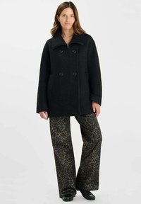 Zwarte dubbelzijdige jas met grote kraag, met een gestructureerde afwerking. Gecombineerd met losse broek met luipaardprint.