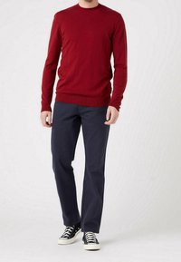Czerwony sweter dzianinowy z okrągłym dekoltem, zestawiony z ciemnonawigacyjnymi chinosami i czarnymi sneakersami wysokimi. Gładka tekstura, luźny krój.