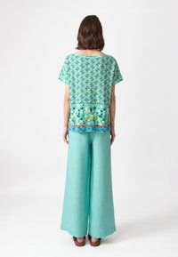 Korte mouw top met een kleurrijk geometrisch patroon in tinten turquoise en geel, gecombineerd met losse mintgroene broek.