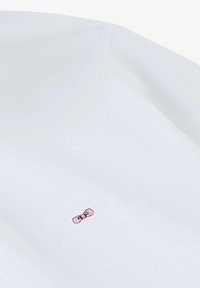 Tissu blanc à texture nervurée avec un détail de broderie de nœud rose légèrement décalé du centre.