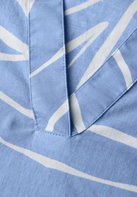Tessuto blu con strisce astratte bianche. Presenta una consistenza croccante e cuciture visibili lungo un neckline a forma di V. Design moderno.