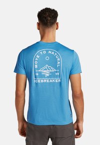Camiseta azul con cuello redondo, gráfico en la parte trasera de montañas y texto en blanco. Mangas cortas, material ligero, corte relajado.