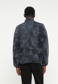 Fleecejacke in Dunkelgrau mit einer strukturierten, plüschigen Oberfläche. Verfügt über einen hohen Kragen und geschnitte Schultern, mit einer lockeren Passform und ohne sichtbare Verschlüsse.