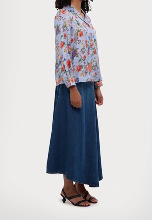 Bluse i lyseblå med blomstermønster og lange ærmer, kombineret med en marineblå denim maxinederdel og sorte sandaler med unikt hældesign.