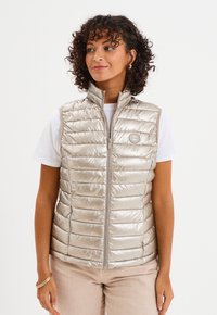 Lekki, bezrękawnik w formie puchowego kamizelki w metalicznym beżu, z poziomym pikowaniem, wysokim kołnierzem, zapięciem na zamek i okrągłym logo.