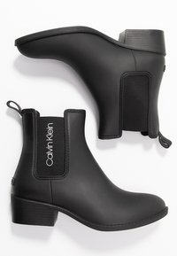 Bottines noires avec une finition en caoutchouc mat, un petit talon bloc, des panneaux latéraux élastiques et une languette pour un enfilage facile. Marque Calvin Klein.