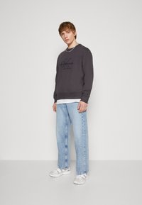 Grijze sweatshirt met het logo "Calvin Klein Jeans", gecombineerd met lichtblauwe wijde jeans en witte sneakers, met een gestructureerde stof.
