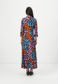 Dolga cvetna obleka z črno podlago, ki vsebuje modre, roza, oranžne in bele cvetove. Zasnova z rokavi do tri četrtine in lahkotna tkanina. Masivni črni škornji.