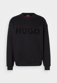 Sweat-shirt noir à col rond avec poignets et ourlet côtelés, arborant un grand logo "HUGO" noir sur le devant.