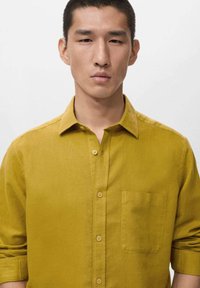 Kurzärmeliges senfgelbes Hemd aus strukturiertem Stoff, mit Tasche auf der linken Seite und einem Button-Down-Kragen.