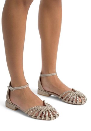 Scarpe flat beige glitterate con un design a strappo, caratterizzate da accenti di strass e un piccolo tacco. Cinghie alla caviglia con dettaglio a fibbia.