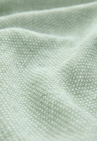 Tela texturizada de color verde claro con un patrón tejido, exhibida en pliegues. La superficie parece suave y ligeramente elevada debido a la textura.